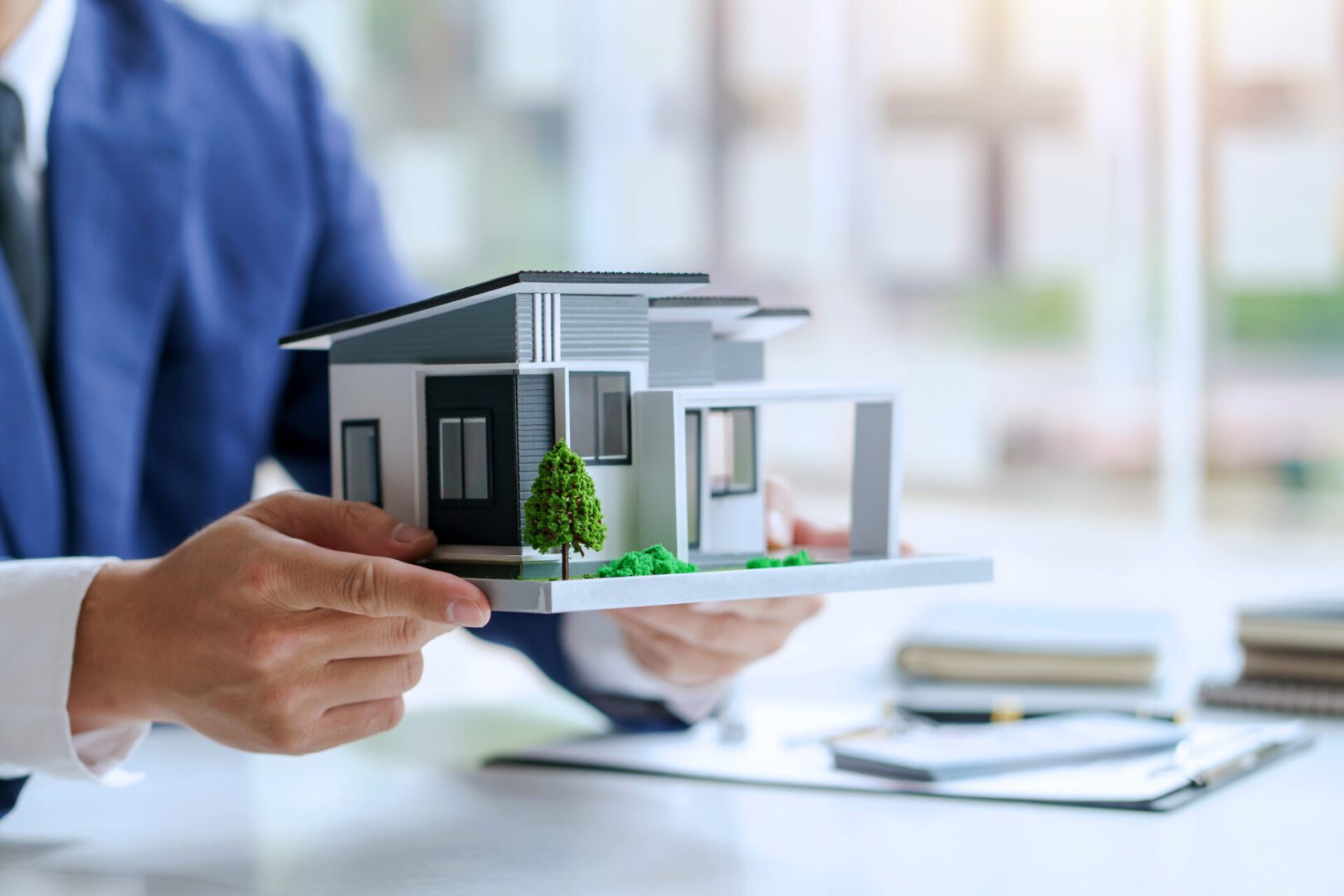 Real estate agent offer house design and contract. Approval of a contract to buy or sell a home. Offers mortgage loans and home insurance concept. Businessman holding miniature house model indoors.